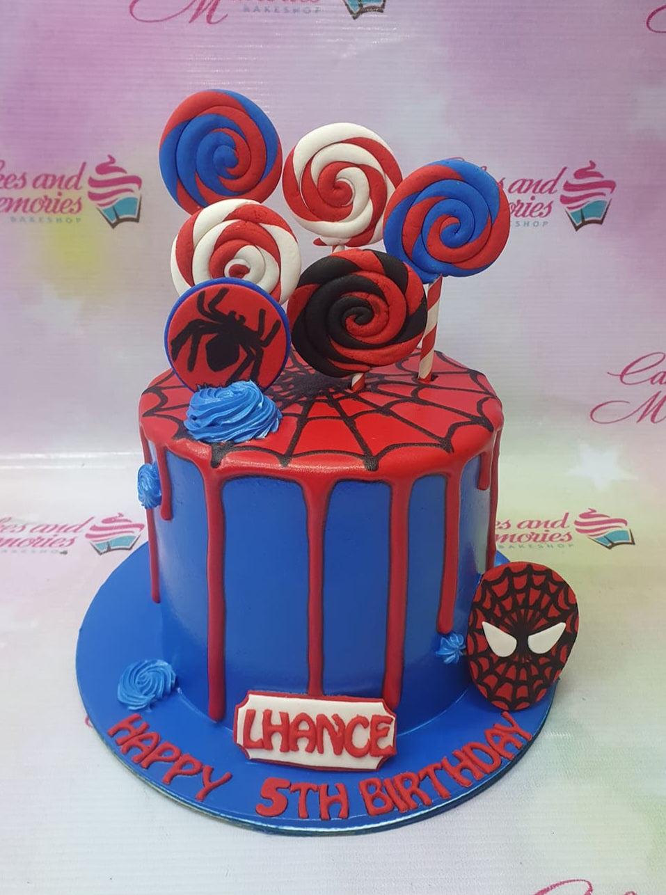 Blue Spiderman themed birthday cake with red drip, spider web top, and fondant lollipops in red, blue, and white.
