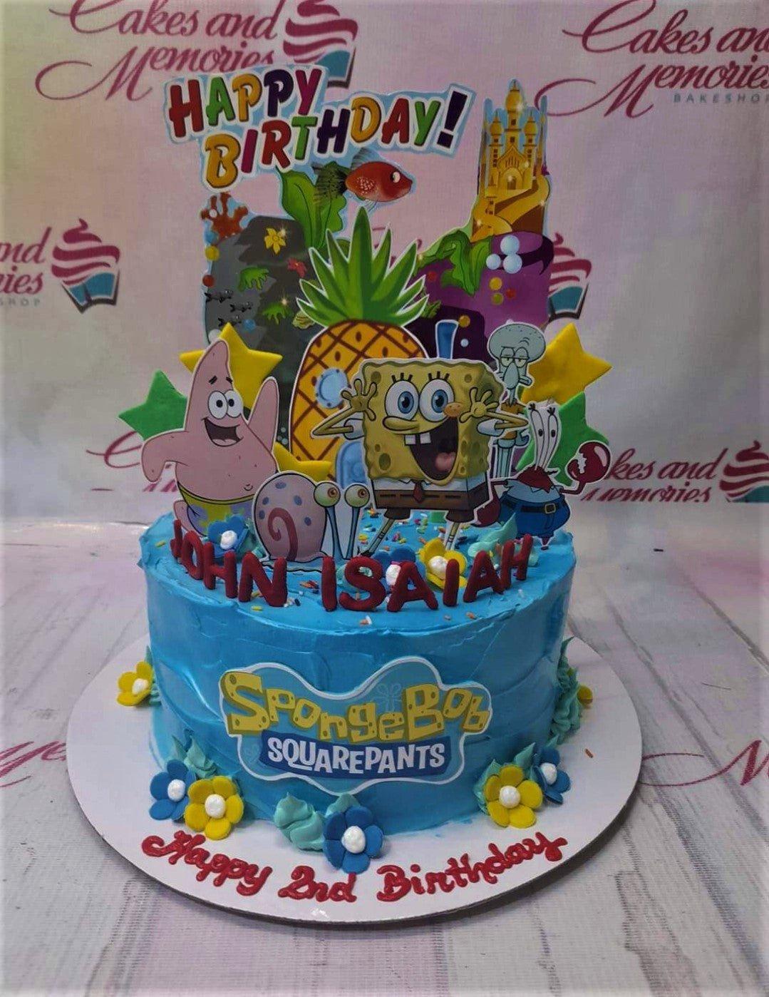 Blue SpongeBob SquarePants birthday cake with character printouts, pineapple house, and colorful icing flowers.