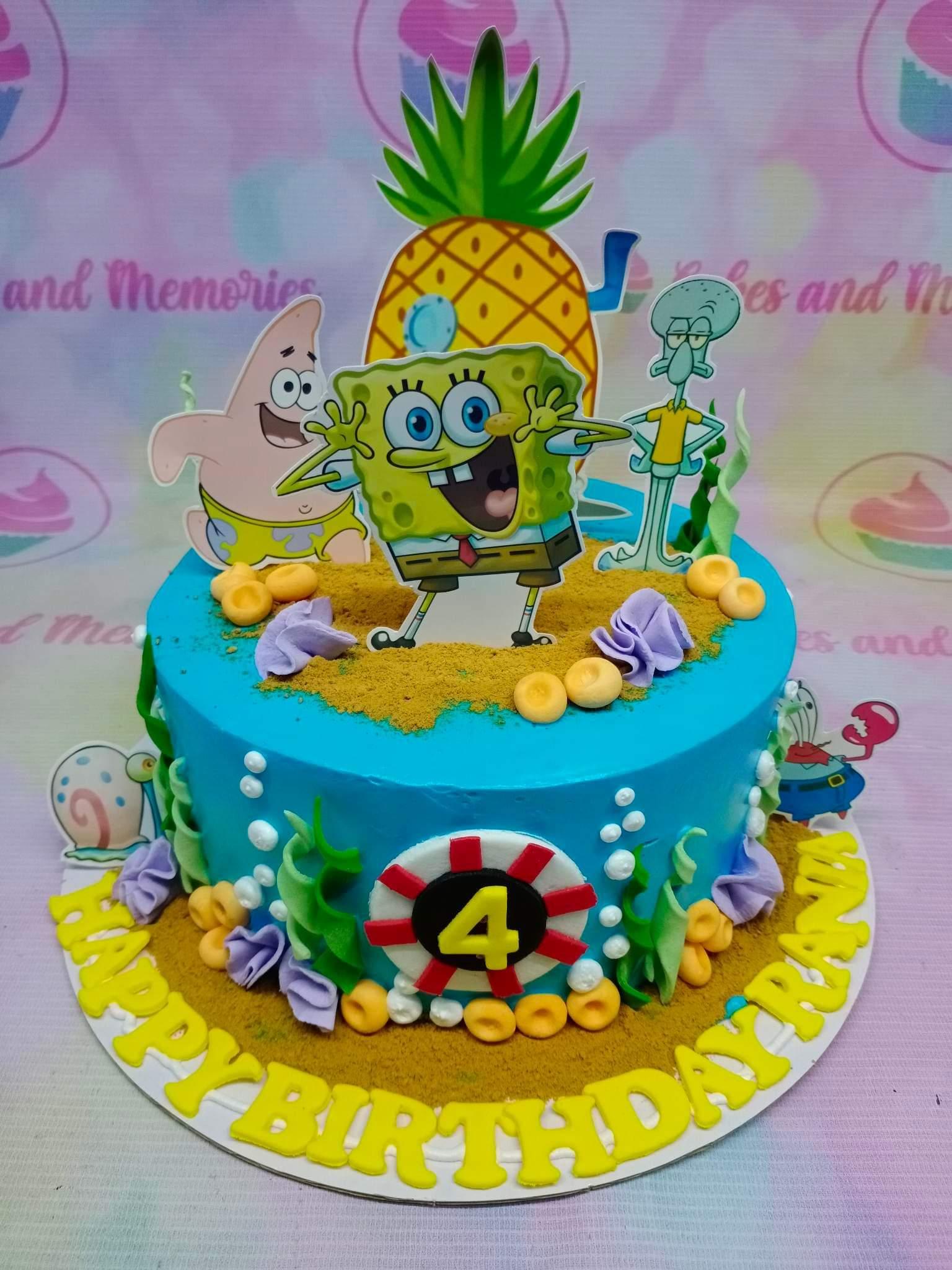 Blue Spongebob Squarepants themed birthday cake with character printouts, edible seaweed, and sand-like crumbs.