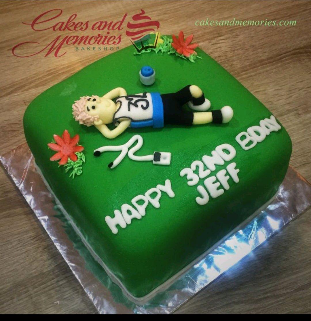 Square green fondant cake for a 32nd birthday featuring a 3D fondant figure of a man lying down with a water bottle and headphones.