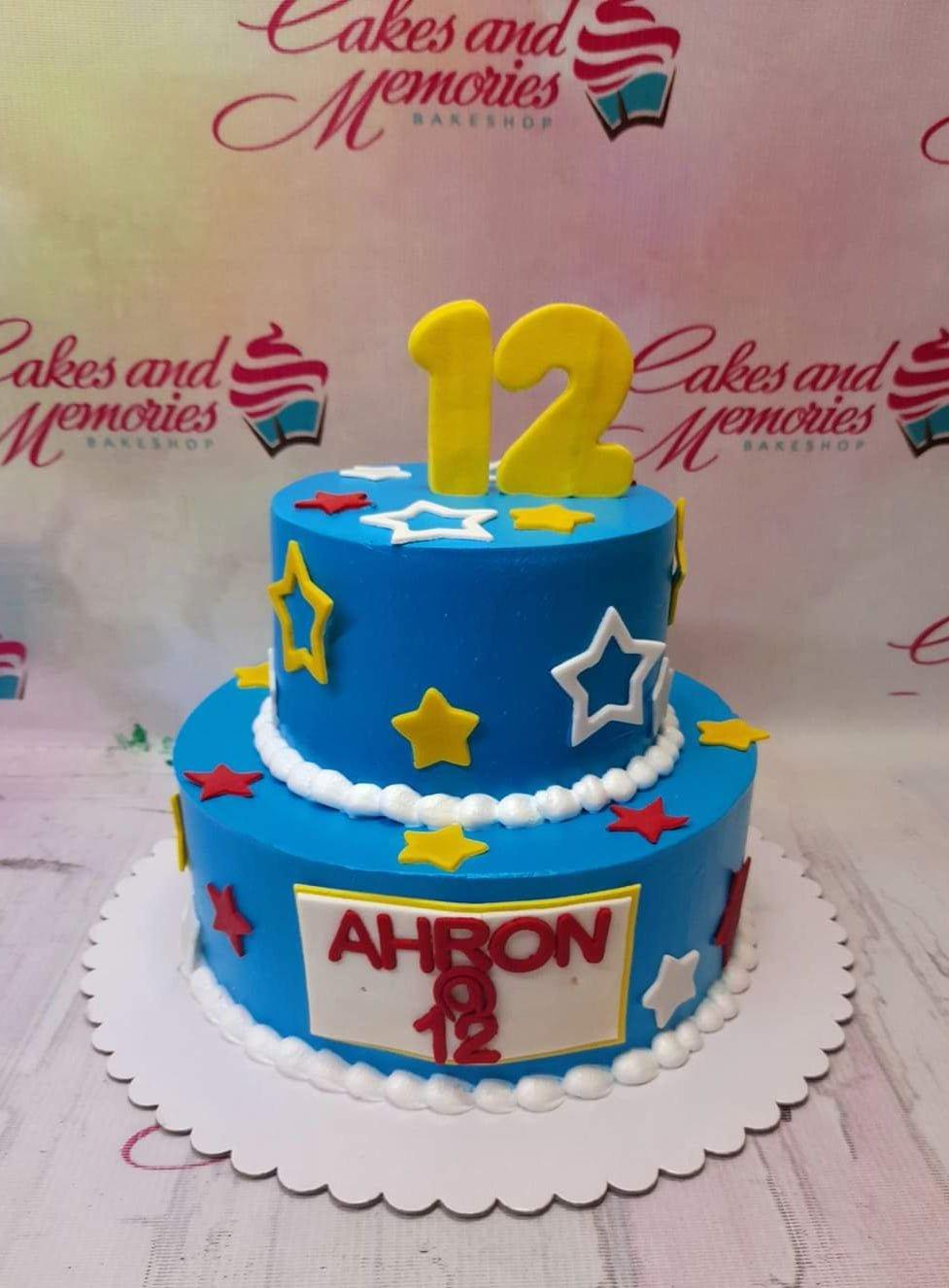 Blue 2-tier birthday cake with yellow, red, and white stars and a large yellow number 12 topper.