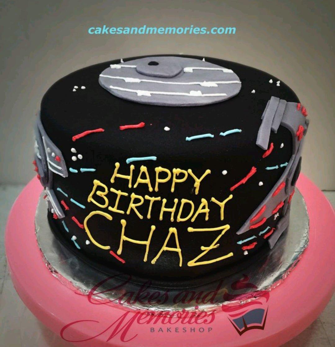 Black fondant Star Wars themed cake with grey Death Star and spaceship details, featuring a yellow Happy Birthday Chaz message.