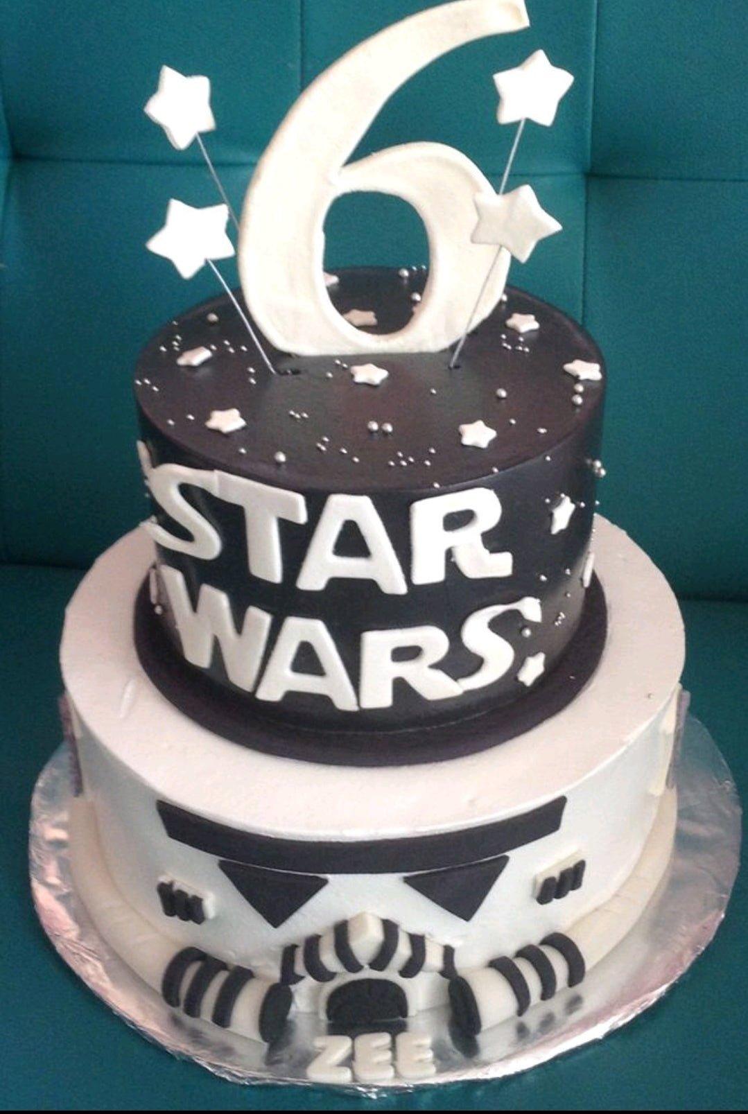 Two-tier Star Wars themed cake with a black top tier featuring the Star Wars logo and a white bottom tier designed as a Stormtrooper helmet.