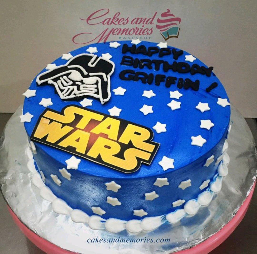Blue Star Wars themed birthday cake with Darth Vader and logo printouts, decorated with white fondant stars and white icing border.
