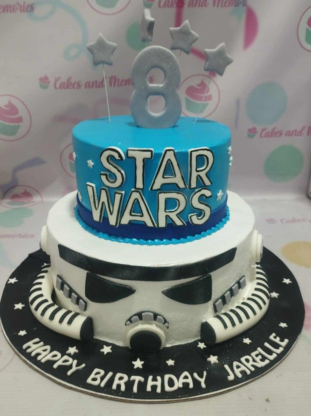 Two-tier Star Wars themed cake featuring a blue top tier with Star Wars logo and a white bottom tier designed as a Stormtrooper helmet.