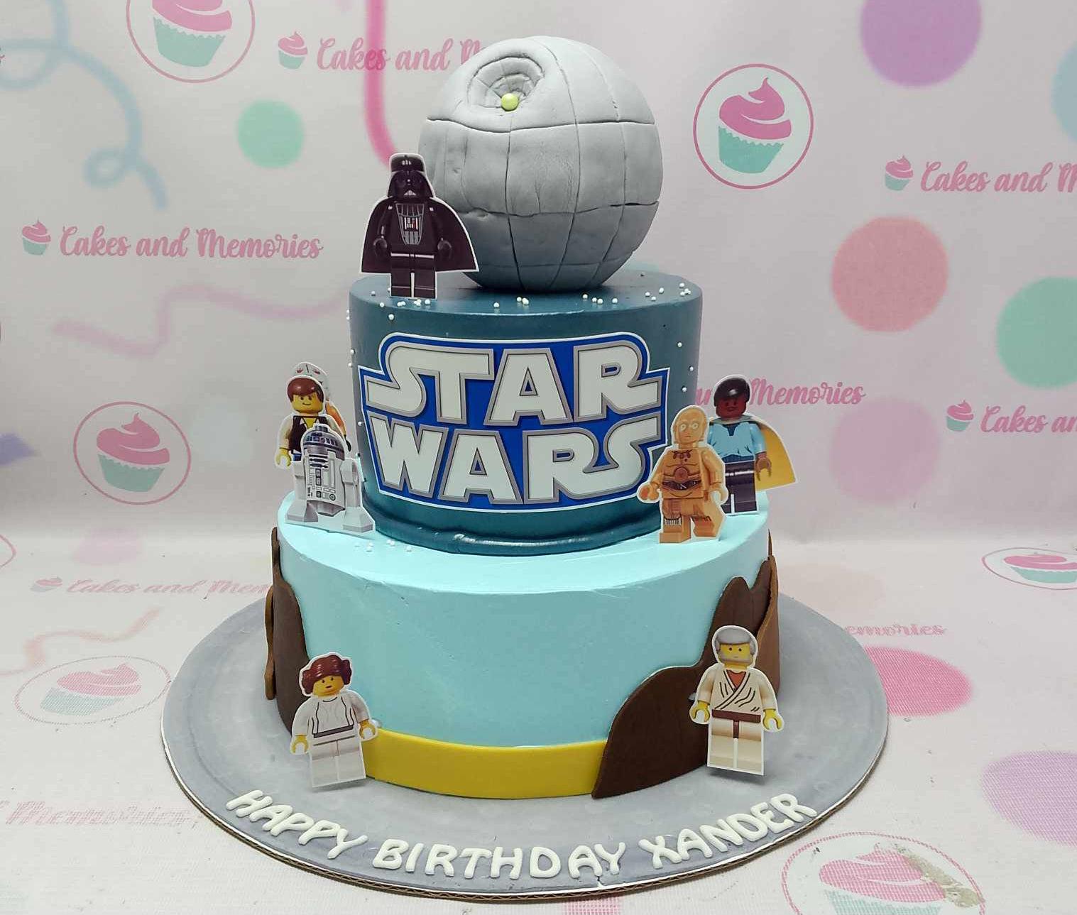 Two-tier Star Wars Lego themed cake with a fondant Death Star topper and various Lego character printouts on blue and light blue tiers.