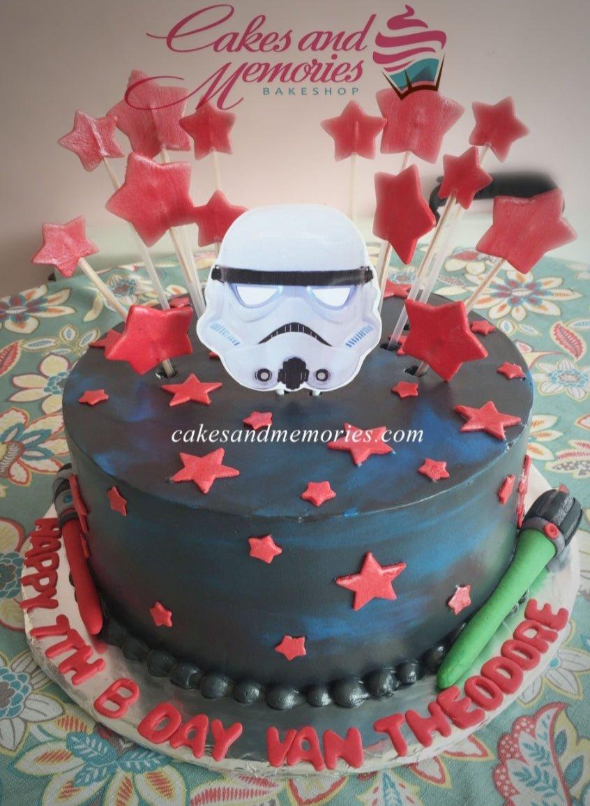 Star Wars Stormtrooper themed birthday cake with red stars and lightsabers on a dark blue galaxy icing base.