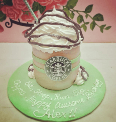 Starbucks coffee cup themed cake with white whipped icing, green bands, and a Starbucks logo printout on a light green base.