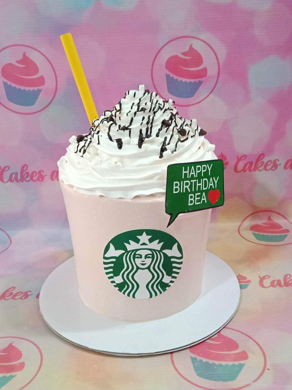Pink Starbucks frappe themed cake with white icing swirls, chocolate drizzle, and a green logo.