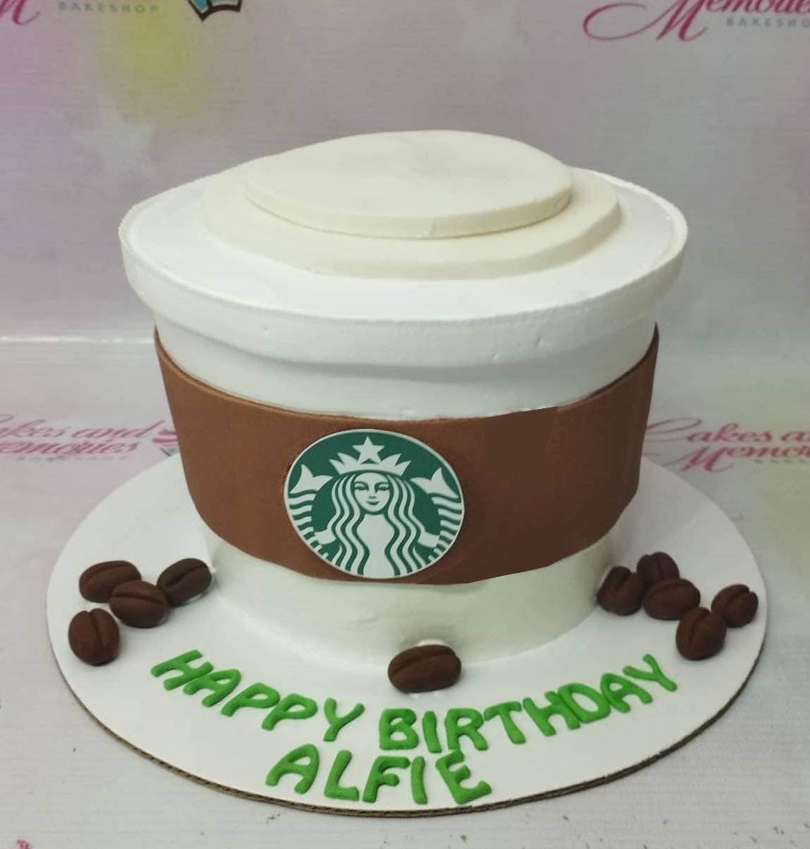 Starbucks coffee cup cake with white icing, brown sleeve, logo printout, and fondant coffee beans on a white base board.