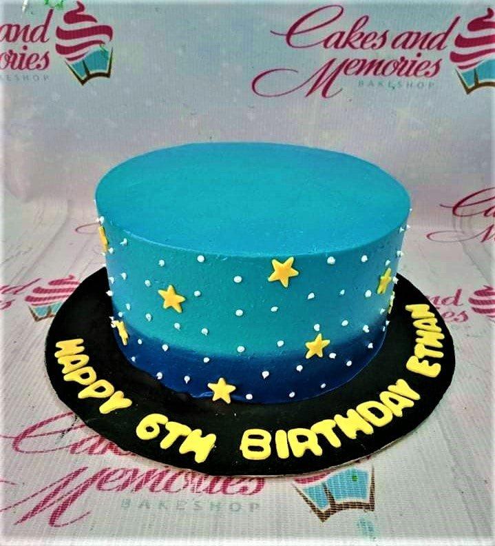 Blue gradient birthday cake with yellow fondant stars and white icing dots, featuring a message on a black fondant base board.