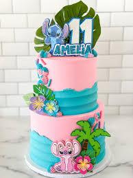 Pink and blue 2-tier Lilo and Stitch themed birthday cake with palm trees, tropical flowers, and character toppers for Amelia's 11th birthday.