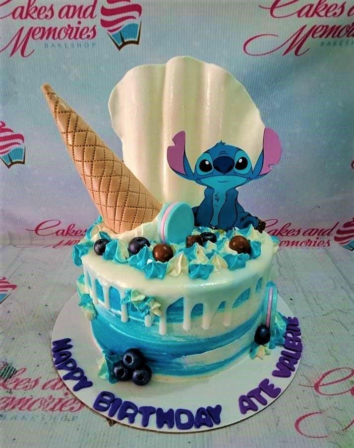 Stitch themed birthday cake with blue and white icing, a large seashell, ice cream cone, and Stitch character topper.