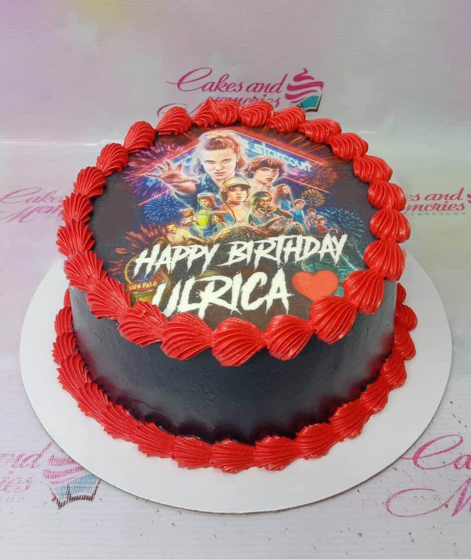 Black round cake with red icing borders and a Stranger Things character printout on top for Ulrica's birthday.