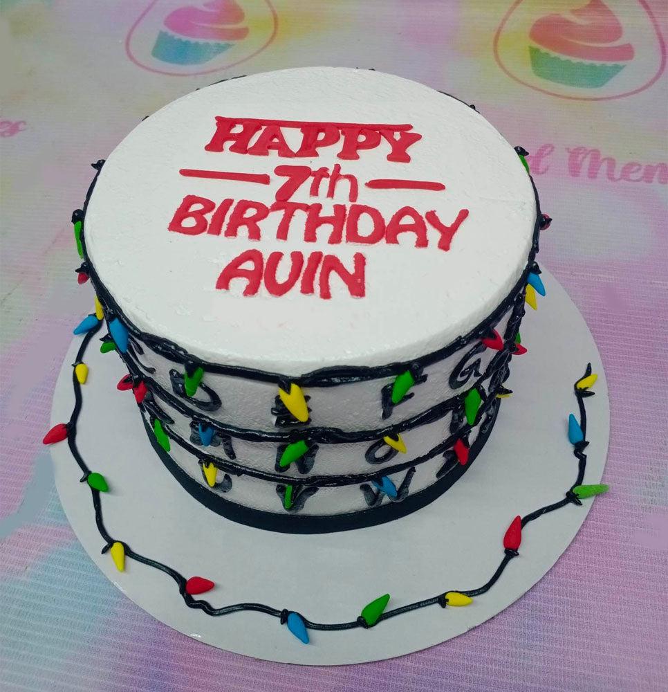 Stranger Things themed birthday cake with white icing, red lettering, and colorful Christmas light bulb decorations.