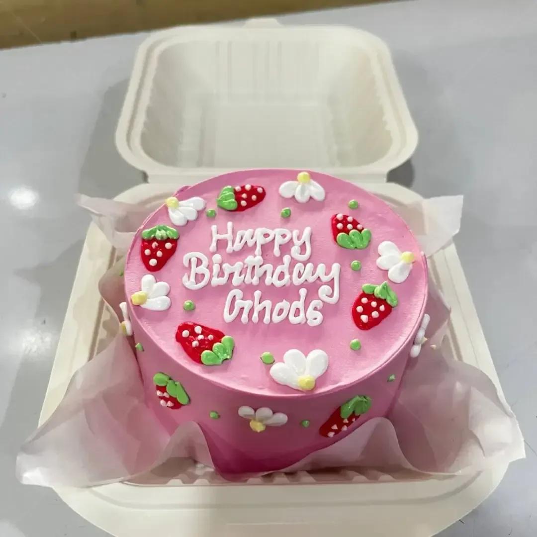 Pink bento cake decorated with white icing daisies and red strawberries with a Happy Birthday message.