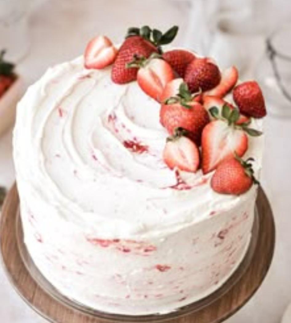 White soft-icing cake with fresh strawberry halves and slices arranged on top and pink strawberry swirls on the sides.