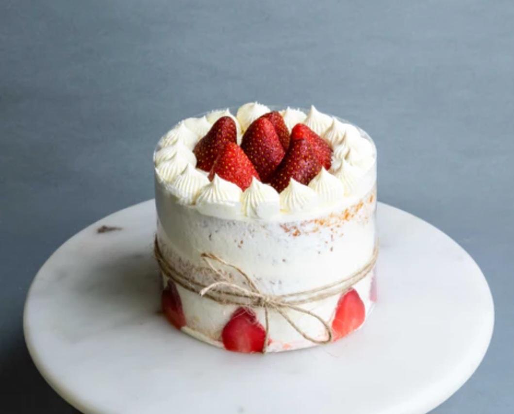 A minimalist semi-naked strawberry cake with white icing rosettes and fresh strawberry slices on top and sides.