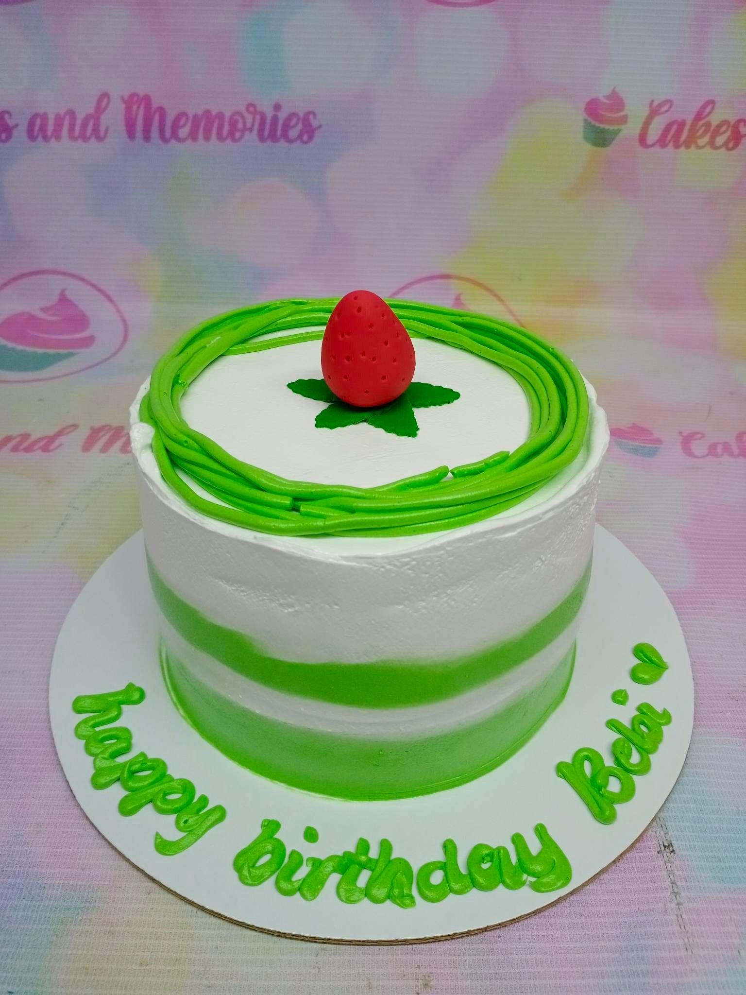 White and green minimalist birthday cake with a fondant strawberry topper and green icing swirls.