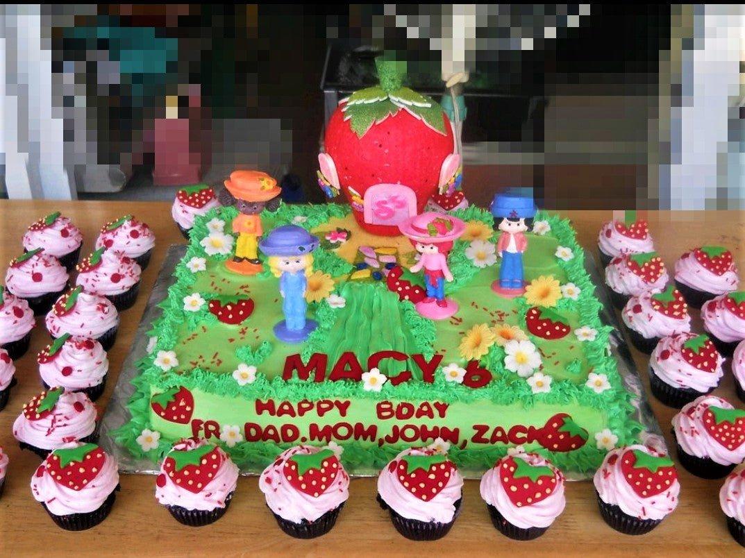 Strawberry Shortcake themed rectangle cake with green icing, strawberry house topper, character figurines, and matching cupcakes.