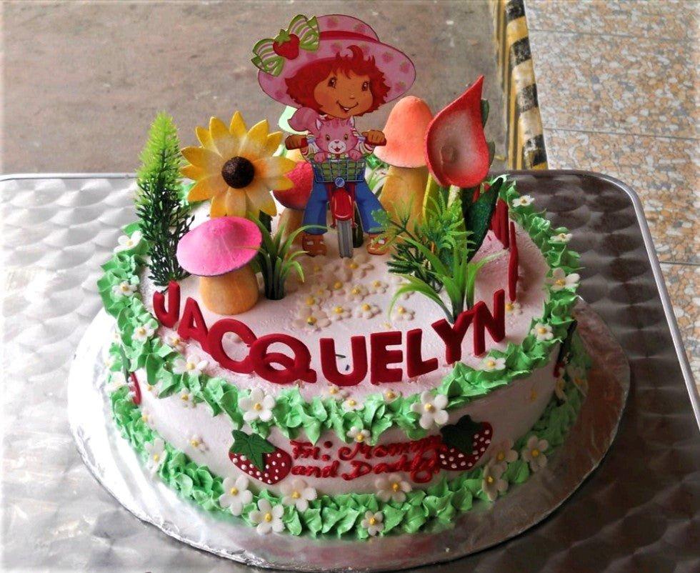 Strawberry Shortcake themed birthday cake with pink icing, green ruffles, and character toppers including Strawberry Shortcake on a bicycle.