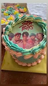 Stray Kids K-pop themed bento cake with teal, pink, and yellow ruffled icing and a group photo printout topper.
