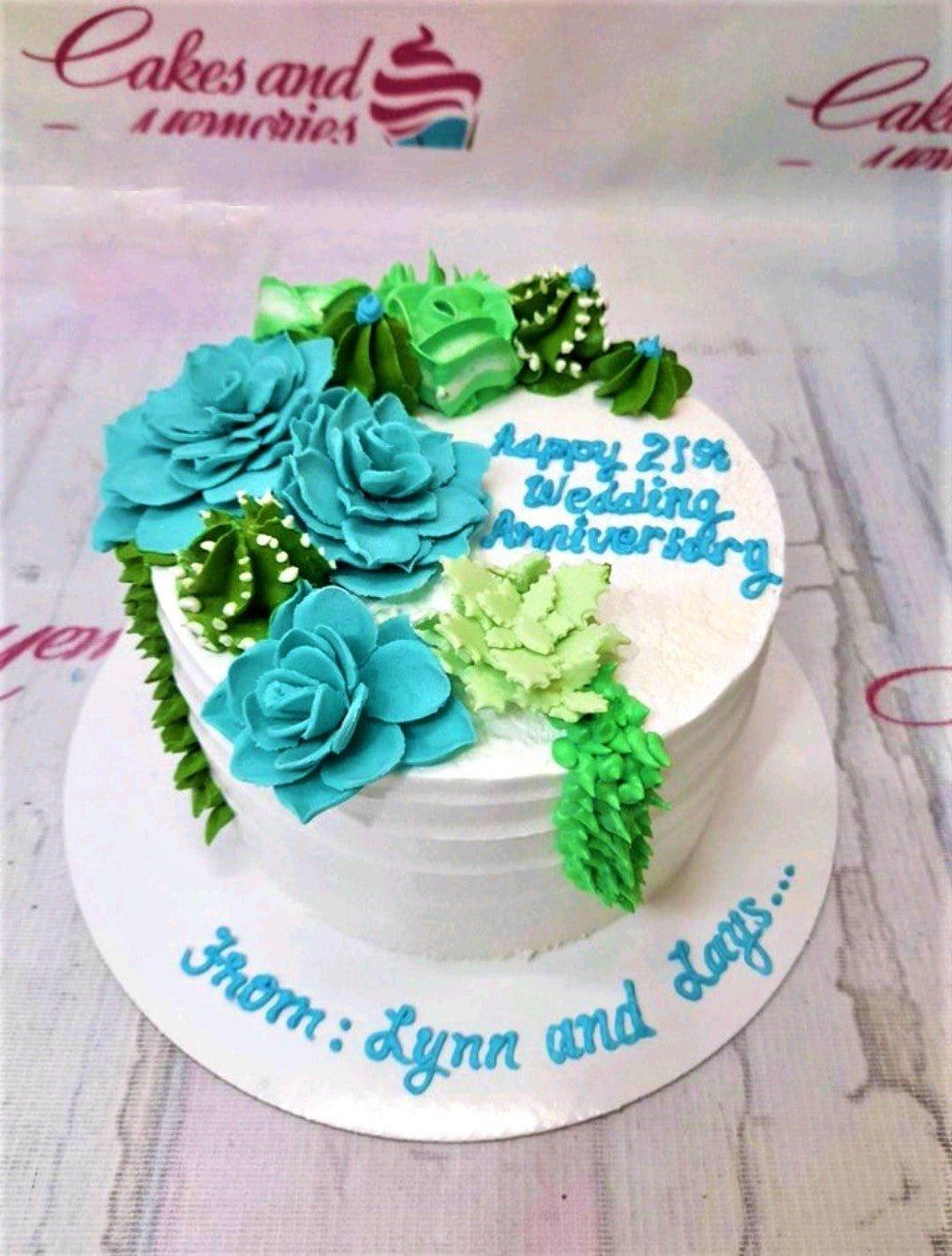 White round anniversary cake decorated with teal and green succulent-shaped icing rosettes and blue piped message.