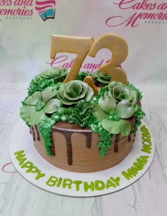 Chocolate drip cake with green succulent icing decorations and a large gold number 73 topper for a birthday celebration.