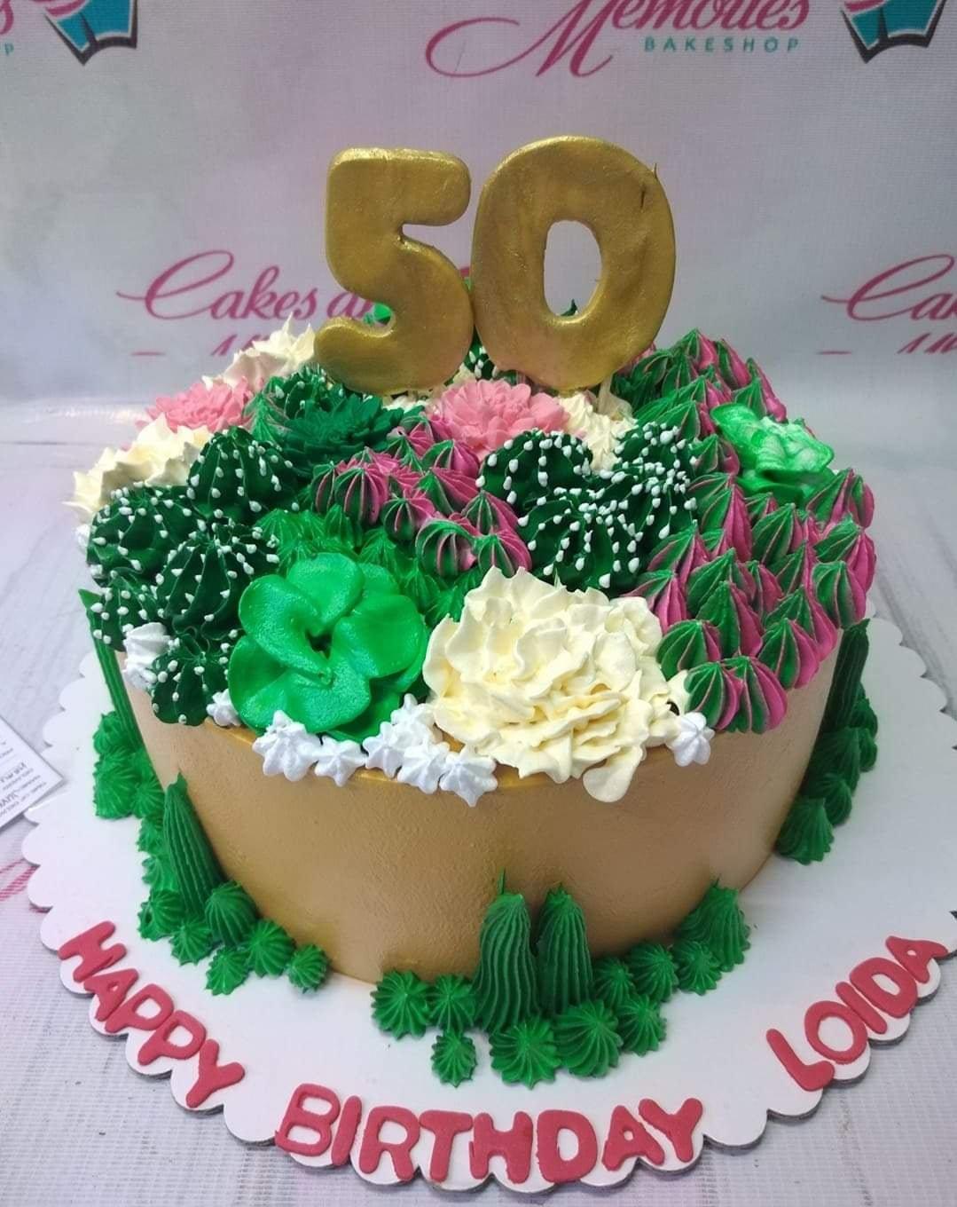 A 50th birthday cake with a gold number 50 topper, decorated with green, pink, and white icing succulents and flowers on a tan base.