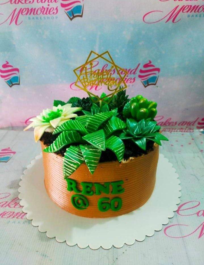 Succulent themed birthday cake with green fondant plants and a gold geometric topper on brown icing.