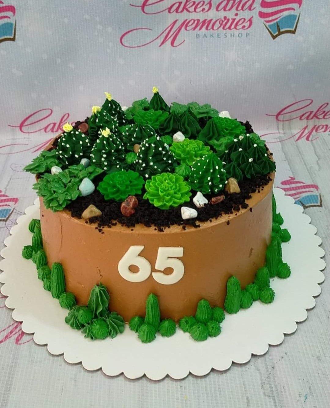 Brown succulent garden cake with green piped icing cacti, chocolate soil, and white number 65 on the side.
