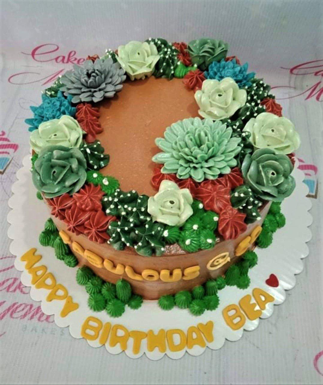 Brown succulent garden cake with intricate green and red icing flowers and a yellow birthday message on the base board.
