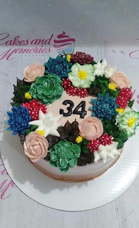 Round birthday cake with a dense garden of colorful piped icing succulents and flowers in pink, green, blue, and red with a black number 34.