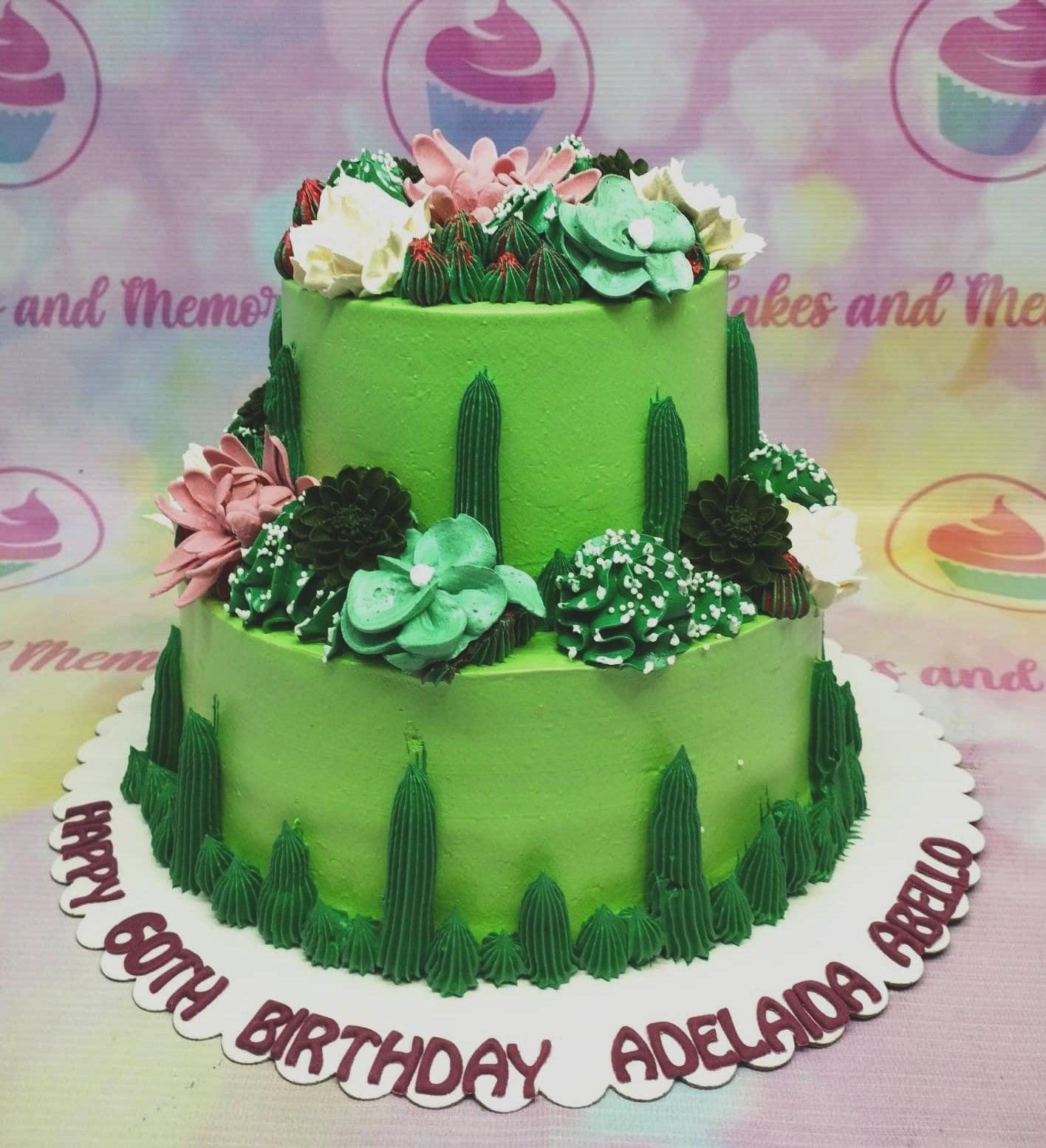 Two-tier green succulent cake with pink and white icing flowers and dark green cactus piping details.