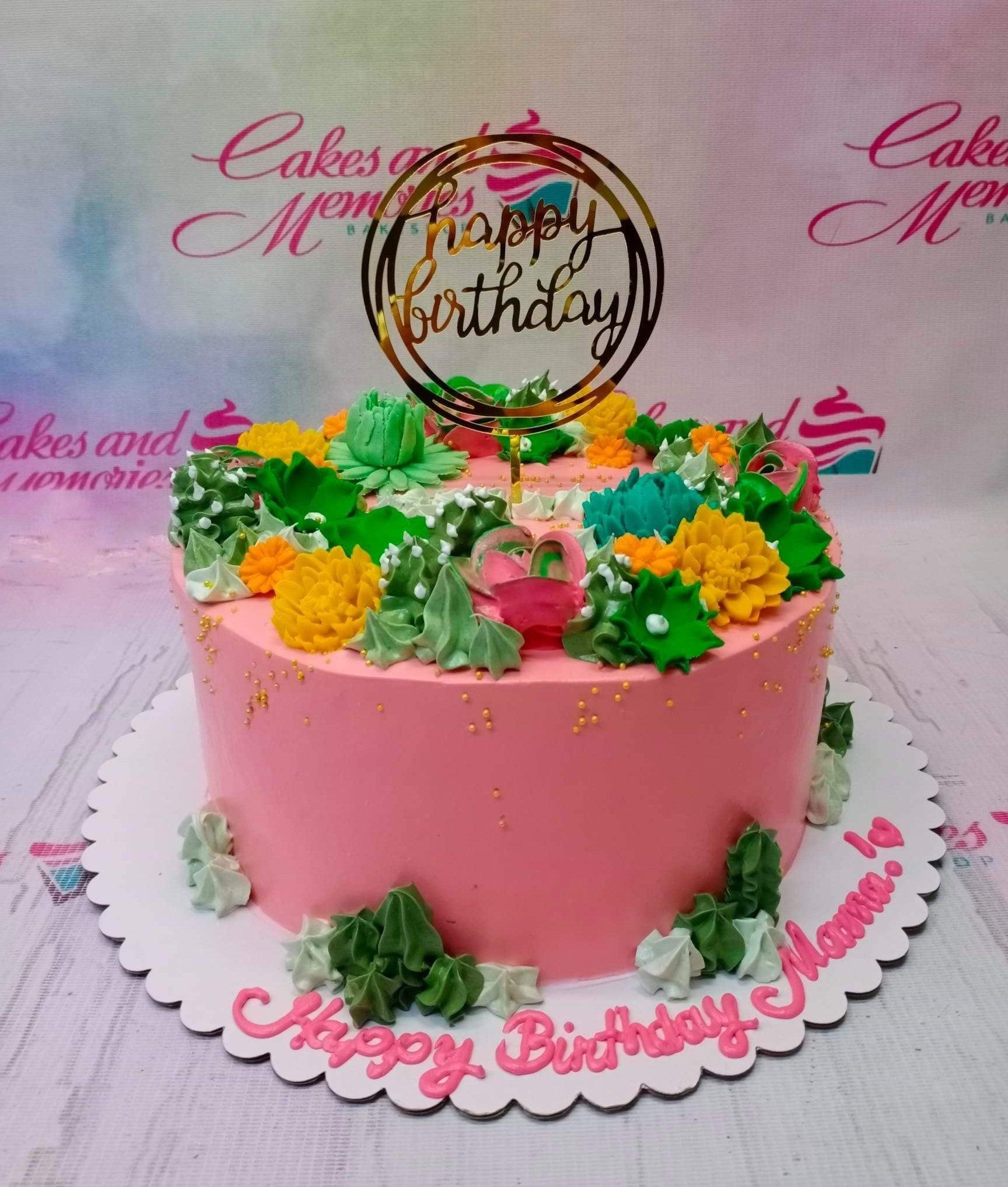 Pink succulent birthday cake with green and yellow icing flowers and a gold Happy Birthday topper.