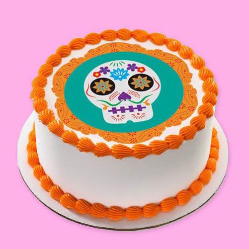 White round cake with orange shell borders and a colorful Dia de los Muertos sugar skull edible print on top.