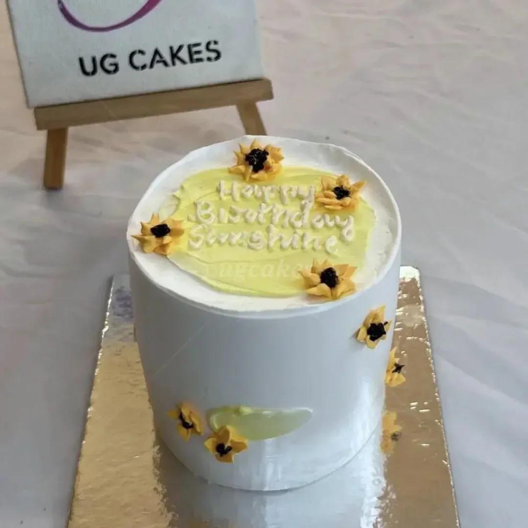 White bento cake with yellow palette knife icing and piped sunflower decorations featuring a Happy Birthday Sunshine message.