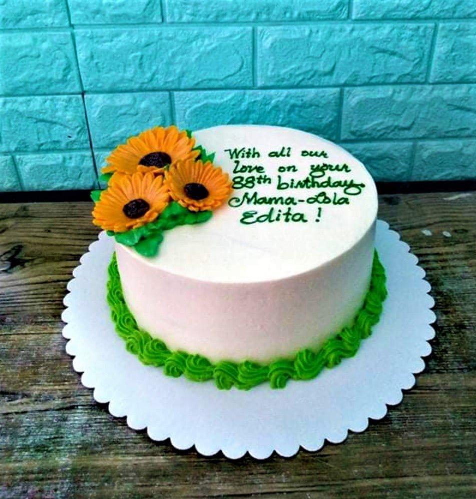 White round birthday cake with three yellow sunflowers and green icing borders for an 88th birthday celebration.