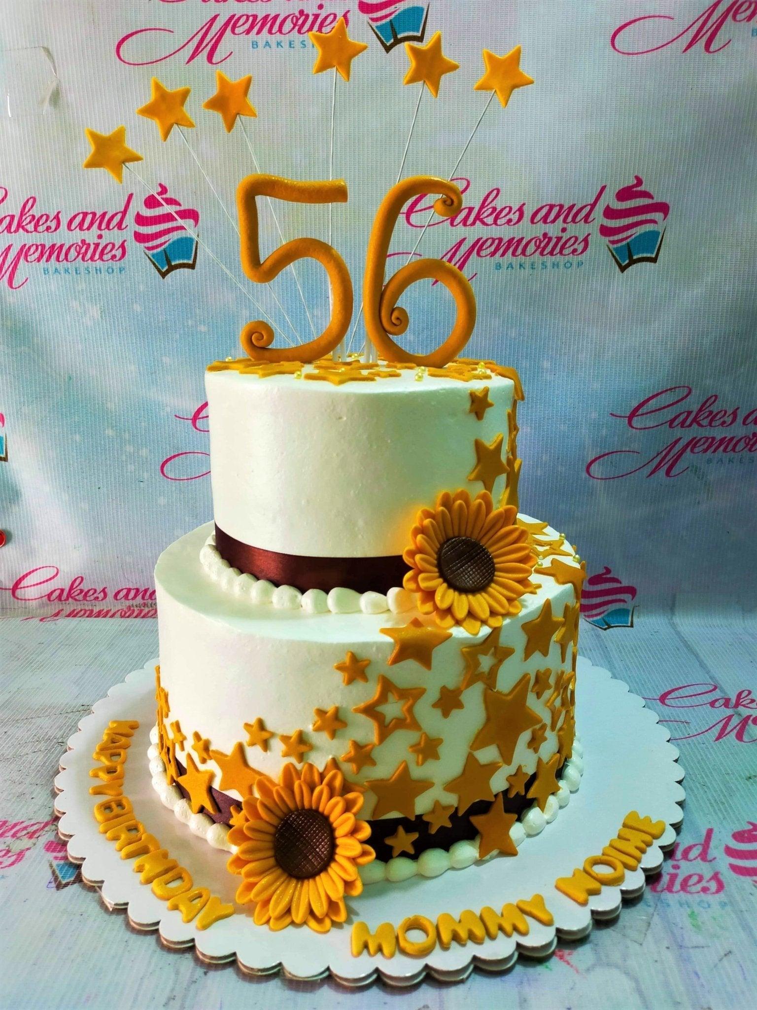 Two-tier white soft icing cake decorated with yellow sunflowers, gold stars, and a large gold number 56 topper.