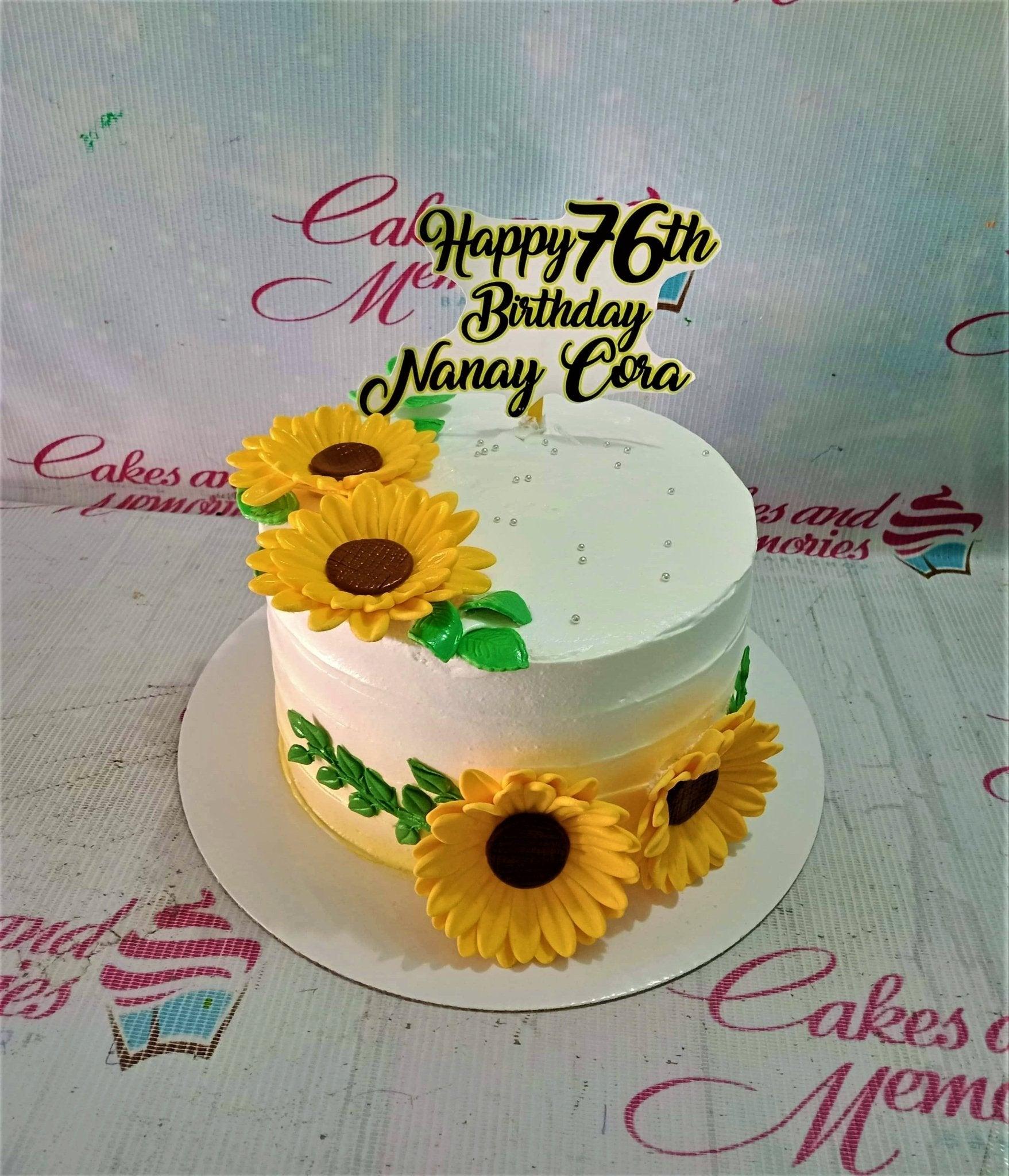 White and yellow sunflower birthday cake with a black and gold Happy 76th Birthday Nanay Cora topper and silver dragees.