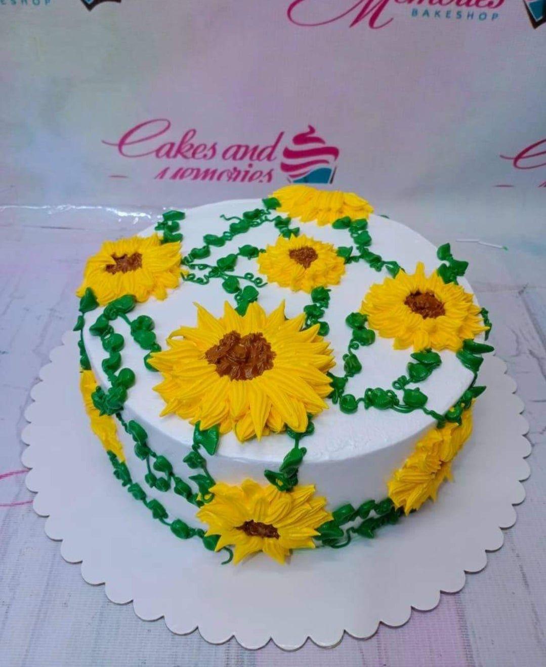 White round cake decorated with vibrant yellow piped icing sunflowers and green vines on the top and sides.