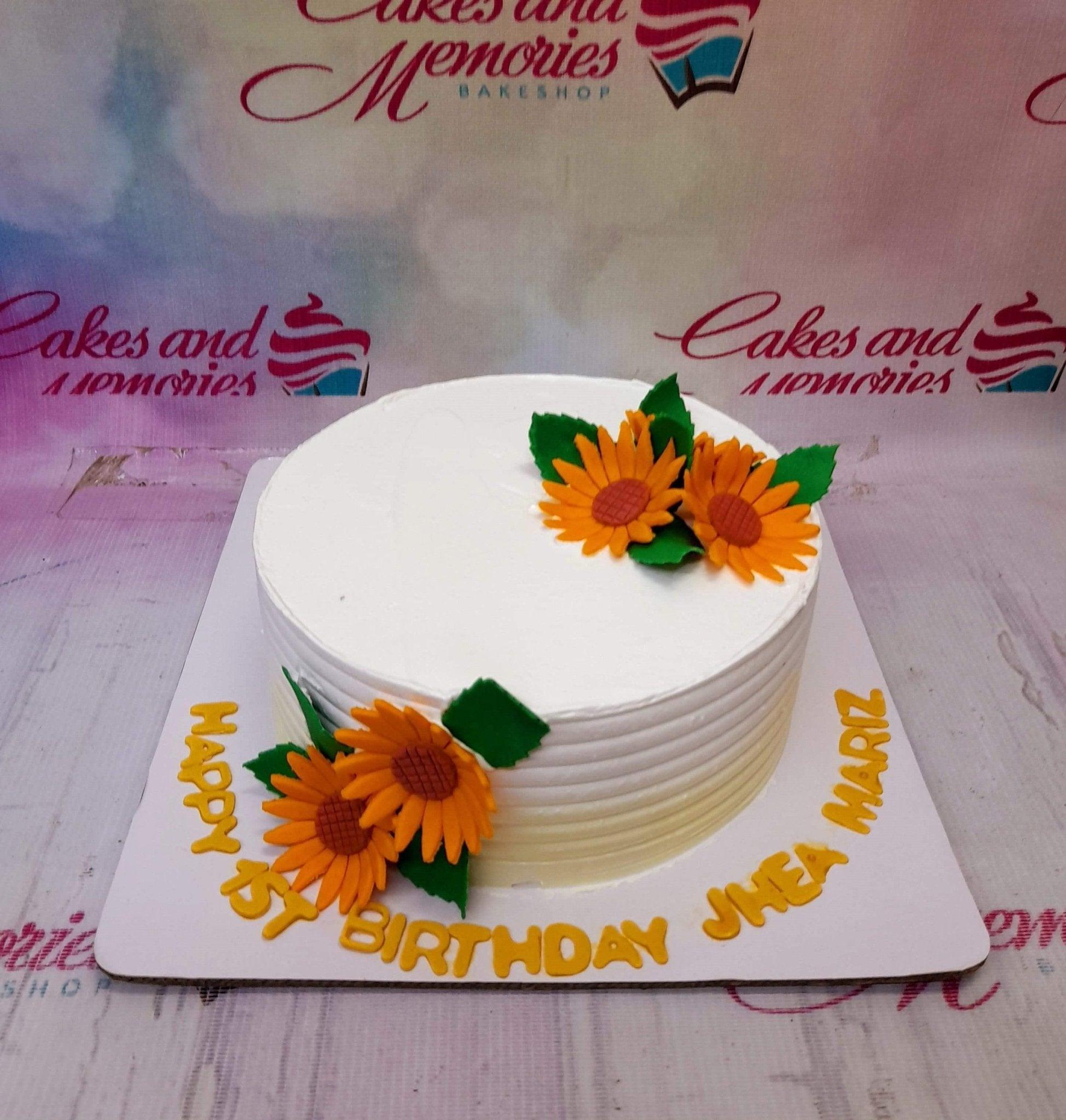 White 1-tier sunflower birthday cake with orange gumpaste sunflowers and yellow gumpaste letters on the base board.