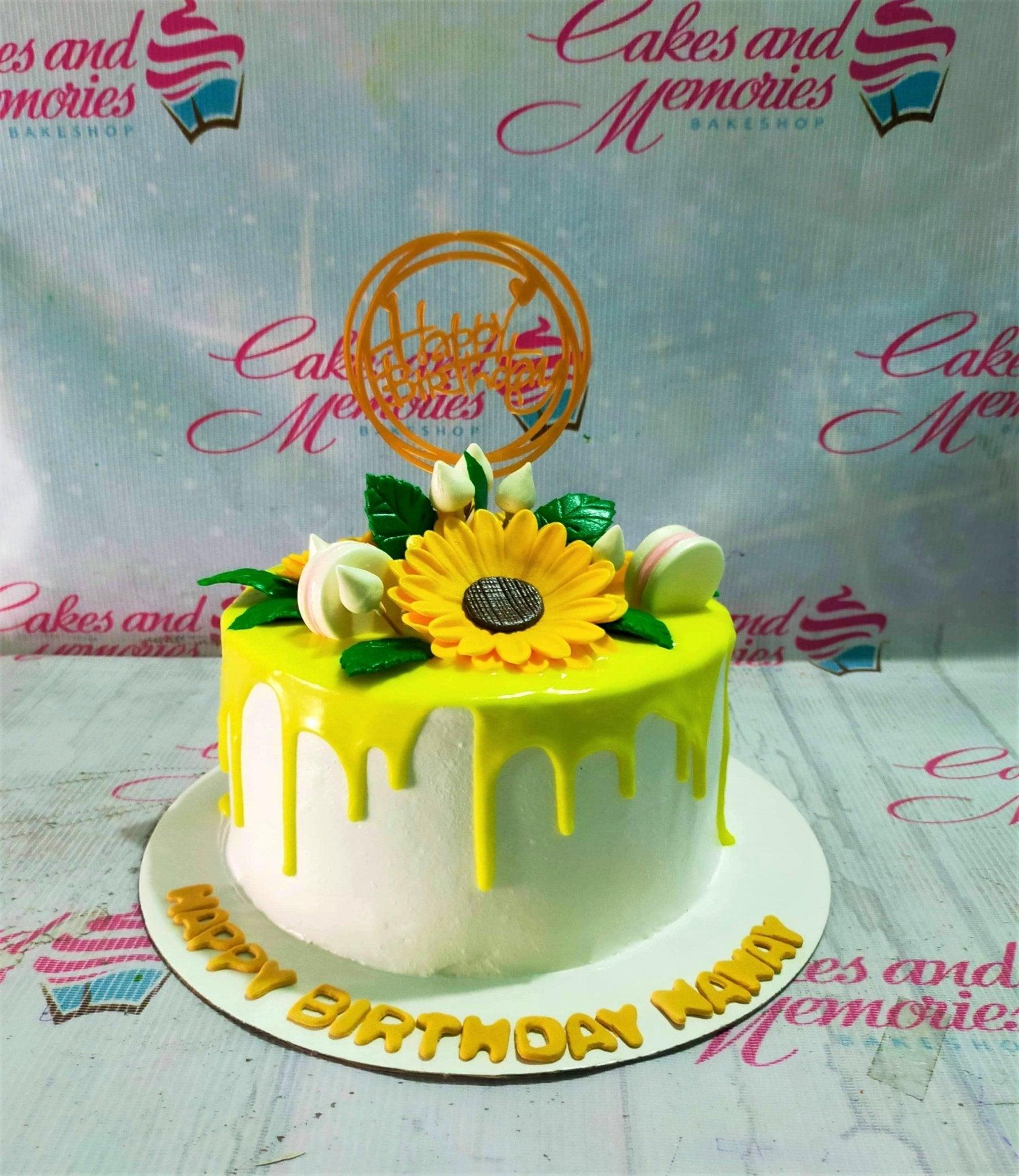 White 1-tier sunflower birthday cake with yellow drip, fondant sunflowers, and a gold Happy Birthday topper.