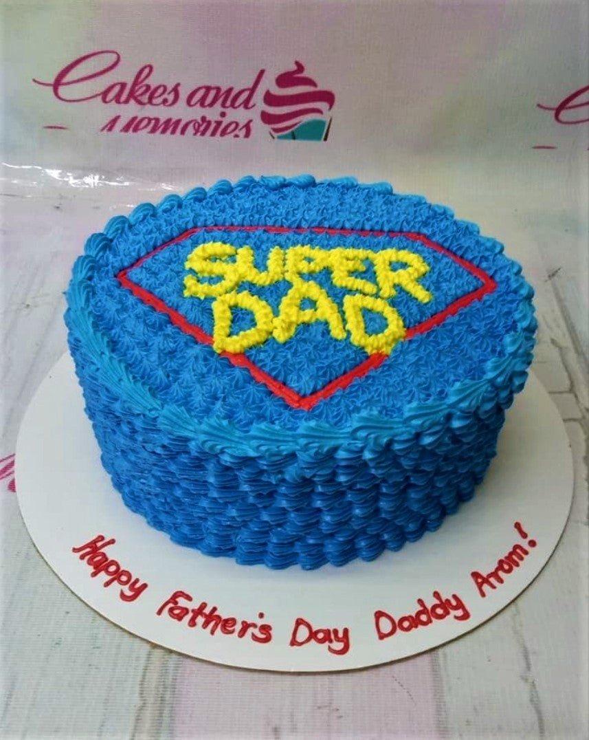 Blue Super Dad cake with red and yellow Superman logo design and piped icing texture.