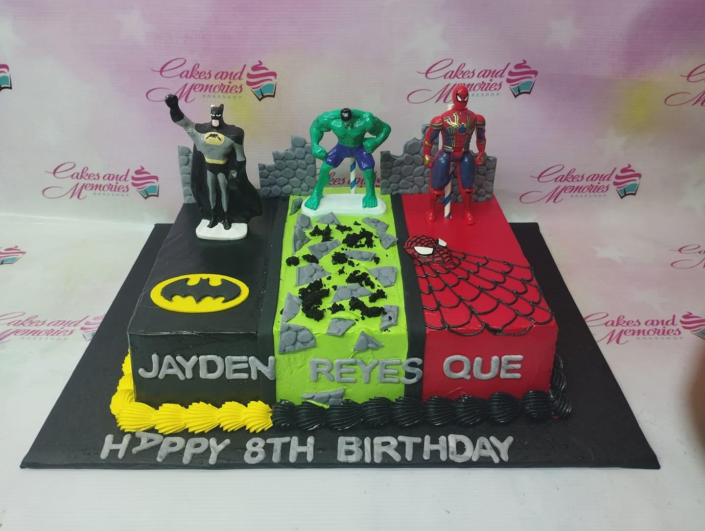 Rectangle superhero birthday cake with Batman, Hulk, and Iron Man toy figures on black, green, and red icing sections.