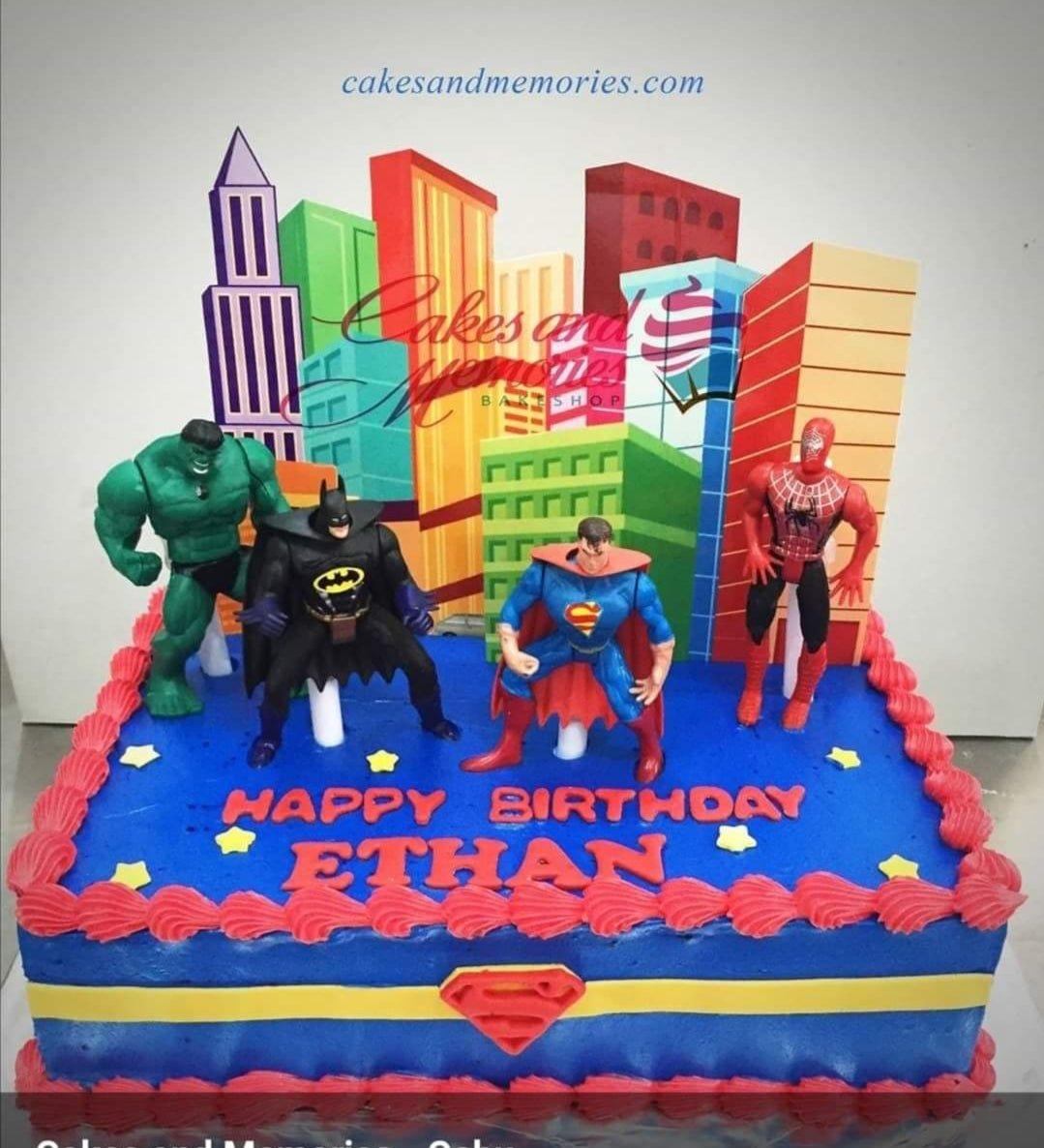 Rectangle blue superhero birthday cake for Ethan featuring Hulk, Batman, Superman, and Spiderman toy figures with a city skyline backdrop.