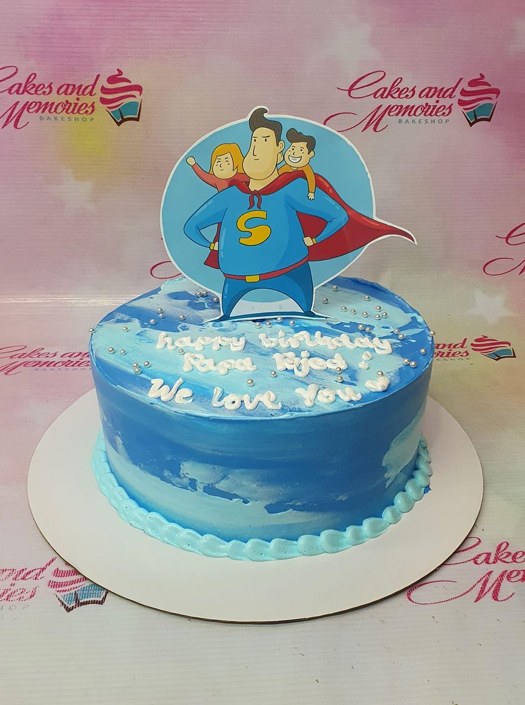 Blue and white marbled 1-tier cake with a superhero dad printout topper and silver dragees.