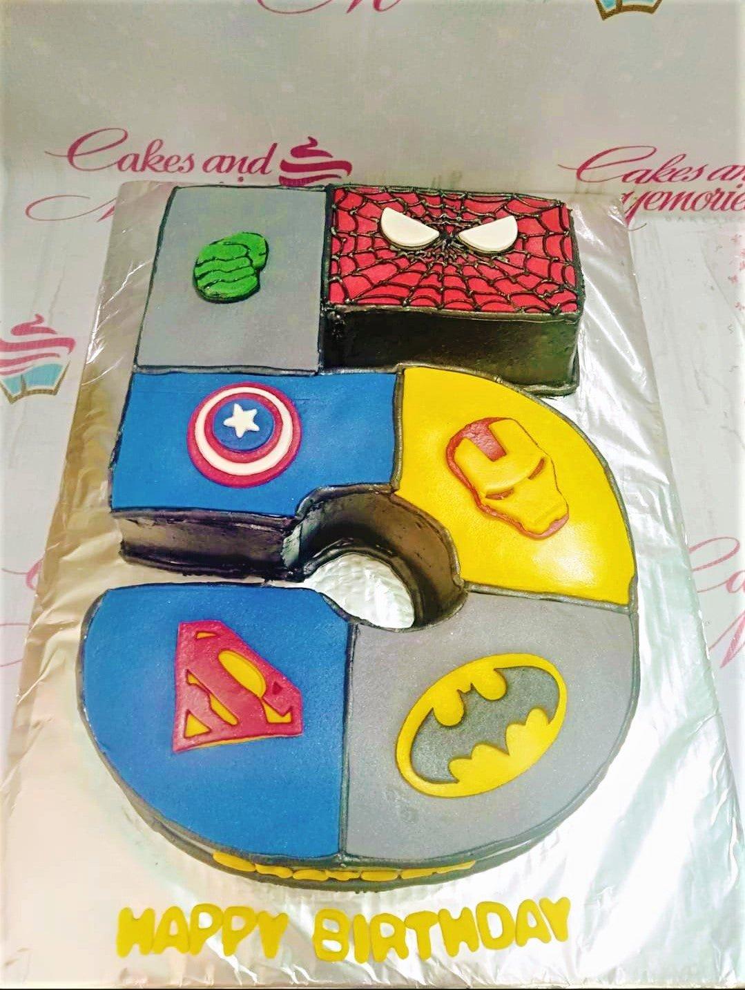Number 5 shaped superhero birthday cake featuring Spiderman, Hulk, Captain America, Iron Man, Superman, and Batman logos.