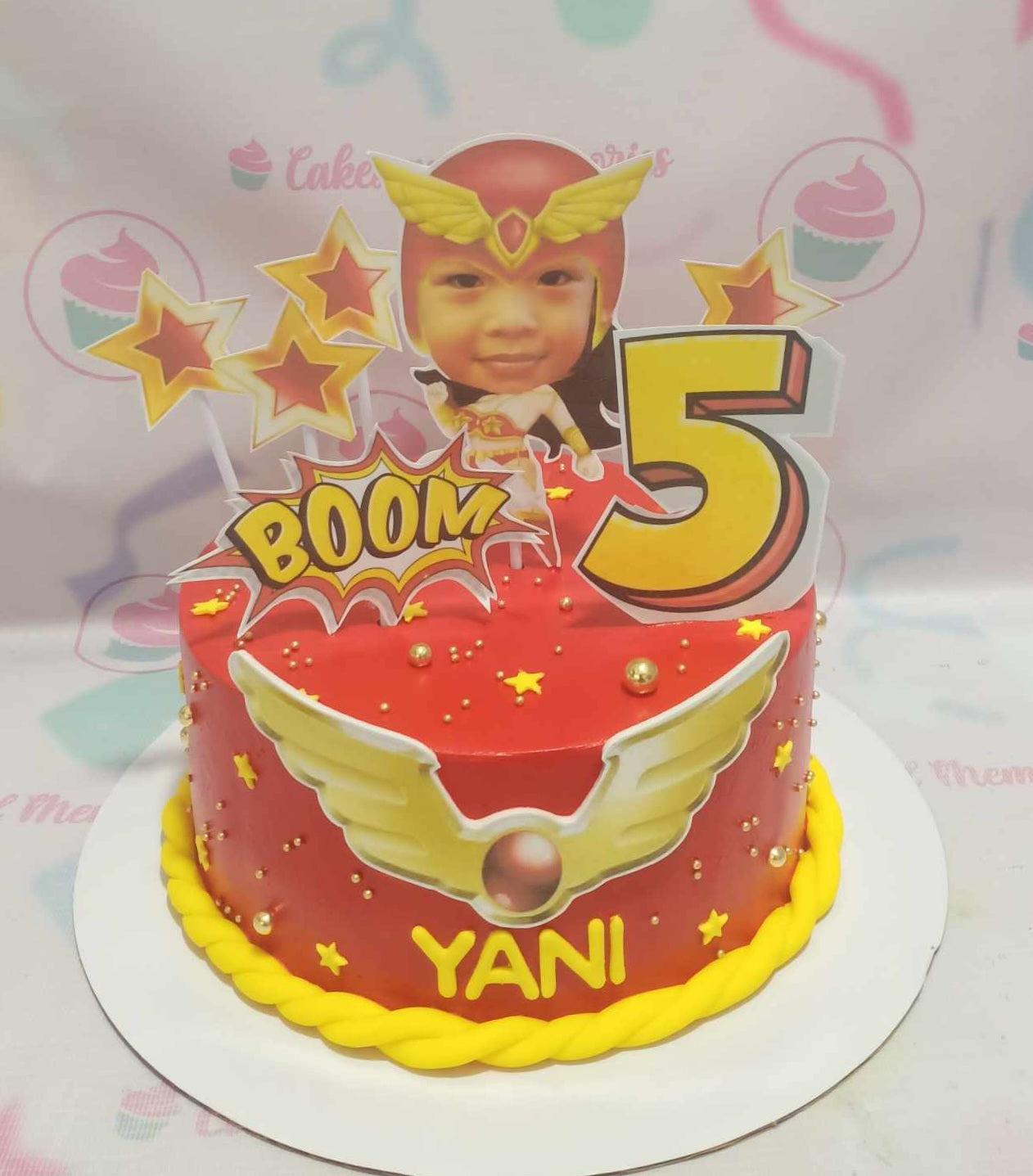 Red superhero themed birthday cake for Yani with a custom photo topper, yellow stars, and gold pearls.