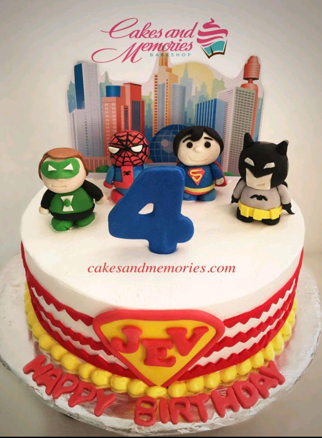 Superhero themed birthday cake with fondant figures of Green Lantern, Spiderman, Superman, and Batman on a white icing base.